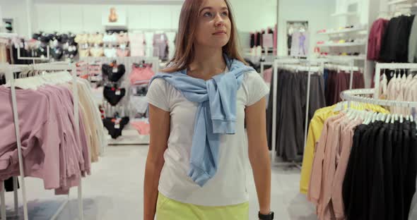 Happy Young Girl is Walking Though a Clothing Store alt