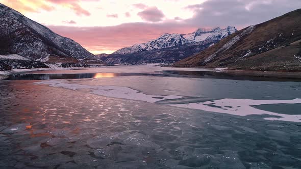 Flying over winter landscape toward snow capped mountain at sunset alt