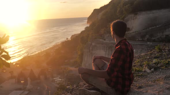 Man Meditates While Sitting on a Rock Against a Beautiful Sunset