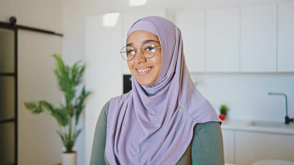 Smiling Muslim Woman in Glasses and Hijab Stands in the Kitchen alt