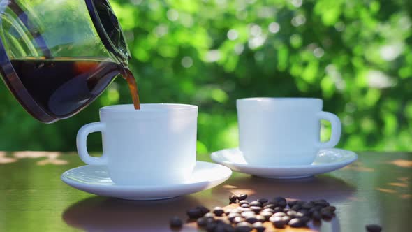 Pouring Coffee Into Two Cups on a Table in a Garden Landscape alt