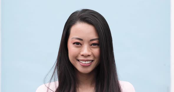 Portrait of smiling Chinese woman, blue wall in the background