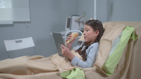 Girl Lie on the Bed, Eat Icecream and Watch Something on Tablet alt