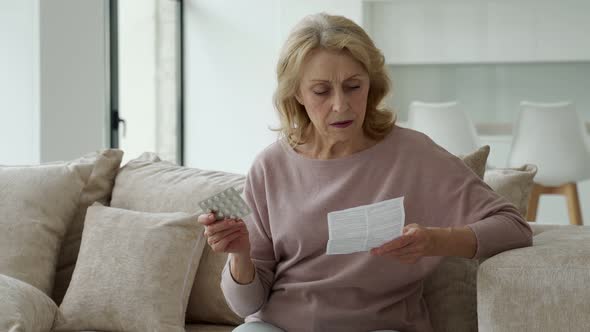 Senior Woman with Pills Reads the Instructions at Home Sitting on the Couch alt