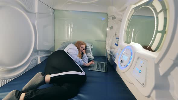 A Girl is Resting in a Pod Hotel Capsule with a Laptop alt