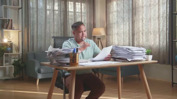 Fat Asian Man Thinking Then Taking Note While Working With Documents At The Office alt