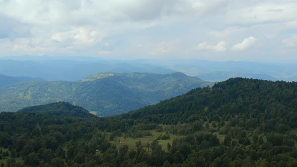 Mountains and green forest from peak of Manzherok under white clouds