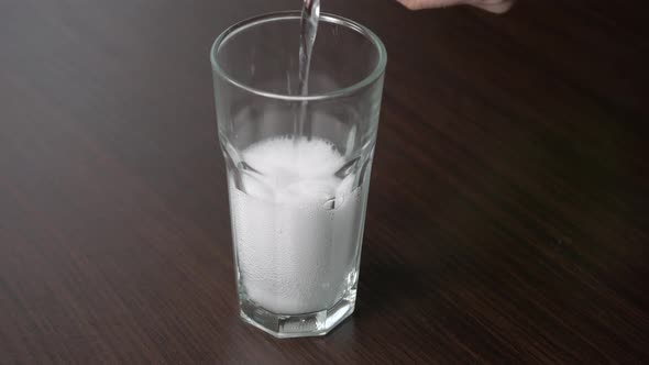 Pouring transparent soda into a tall glass on a wooden table alt