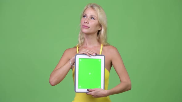 Young Happy Beautiful Blonde Woman Thinking While Showing Digital Tablet