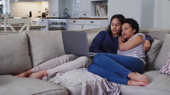 Mixed race lesbian couple sitting on couch and alt