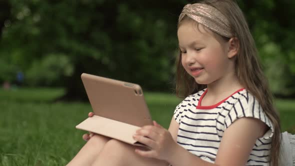Funny Girl 67 Years Old Sits on the Grass in a Summer Park with a Tablet alt