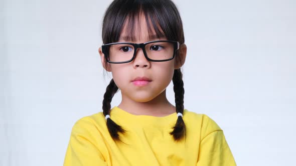 Angry girl with glasses and a yellow t-shirt stands with her arms crossed against a white background alt