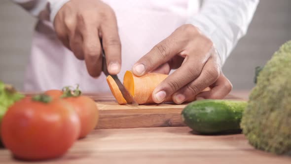 Young Man Cutting Fresh Carrots on Chopping Board on Table alt