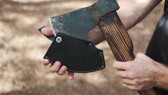 The guy in the forest close-up opens a sharp ax. Removes the leather sheath from the blade alt