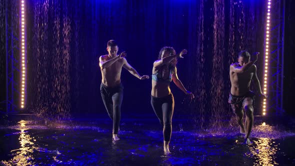 Capoeira. A Young Woman and Two Men Practice Martial Art with Dance Elements in the Rain in a Dark alt