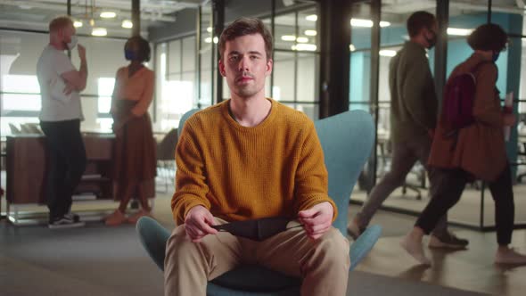 A Young Handsome Guystudent is Sitting in a Protective Mask on His Face and Looking at the Camera alt