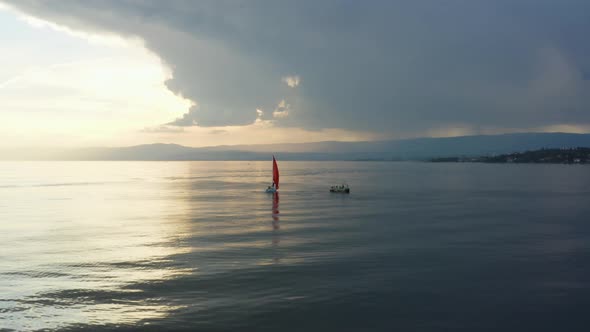 Aerial orbiting around sailboat changing tack at sunset. Dark storm-clouds in the backgroundLake, L alt