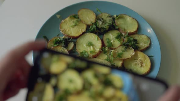 Woman makes photo of cut potatoes with parsley on plate