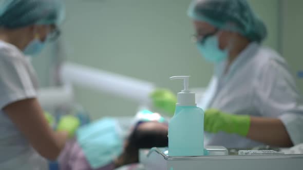 Disinfectant in Dental Office with Blurred Doctor and Assistant Curing Patient at Background alt