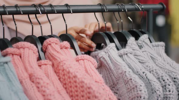 Clothing Store Closeup of Clothes Hanger with Bright Colored Sweaters Female Hands of Unrecognizable alt
