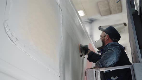 Closeup of a Paint Line Worker in a Respirator Sanding the Car Wall Before Finishing Painting Using