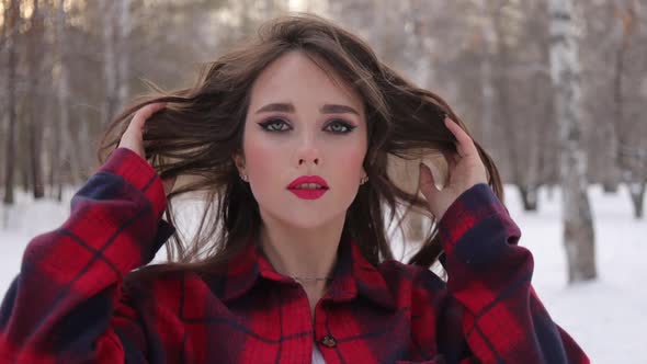 Young Woman with Wavy Hair Standing and Touching Face in Winter Forest