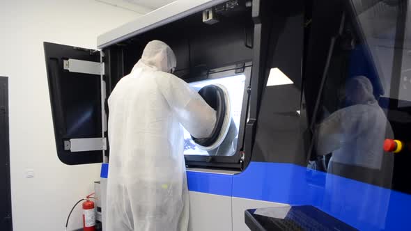 A Man in a White Protective Suit Stands Near a Large 3D Printer alt