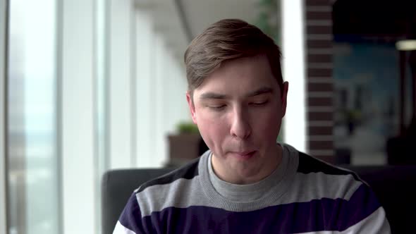 A Young Man Is Eating a Burger. A Man Sits in a Cafe By the Panoramic Window and Eats Fast Food. alt