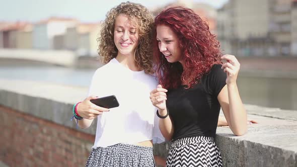 Two happy girls looking at smart phone with city on background alt
