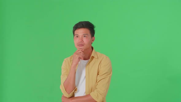 Young Asian Man Thinking About Something Then Raising Her Index Finger In Green Screen Studio alt