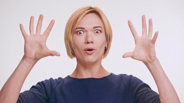Middleaged Caucasian Blonde Female in Blue Sweatshirt Making Faces Jokingly on White Background alt