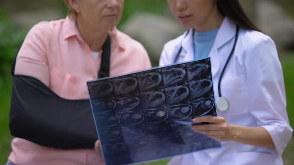 Young Physician Showing X-Ray Image to Mature Female Patient Wearing Arm Sling alt