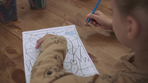 A Student Girl Paints a Drawing with a Colored Pencil While Sitting at the Table alt