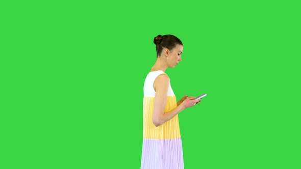 Young Beautiful Girl in Whiteyellow Dress Walks Typing on Mobile Phone on a Green Screen Chroma Key alt