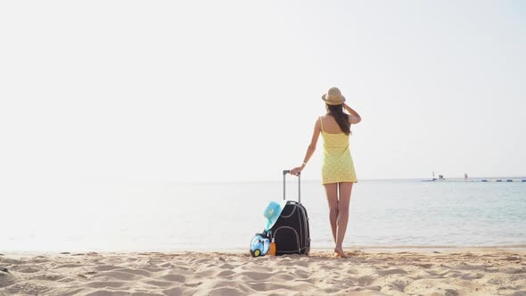 Beautiful Woman in a Hat with Suitcase Against the Sea During Summer Travel Vacation alt