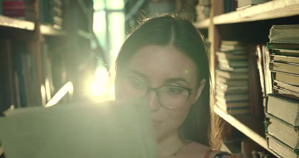 Girl in Glasses Admires of the Book and Flips Through It with Joy in a Library alt