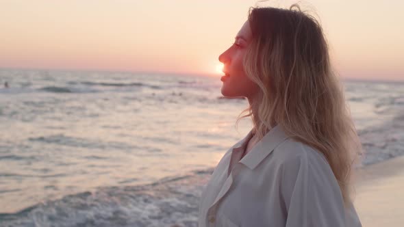 Young Blonde Woman with Wavy Hair Standing on Beach By the Sea on Sunset