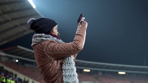 Girl Dressed in Hat and Scarf Shooting Video at the Stadium alt