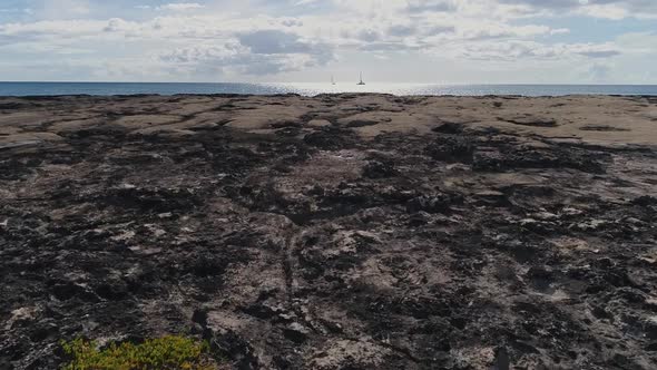 Drone flying low over volcanic rocky shore, towards pacific ocean, Sunlight reflection on Water. alt