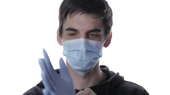 Portrait of a Young Man in a Medical Mask Who Puts on Medical Gloves on White Background