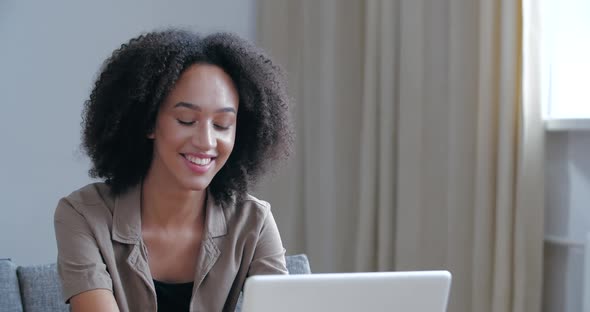 Attractive Young Afro Girl Sitting with Laptop Typing Smiles at Camera Showing Hand OK Sign, Agree alt