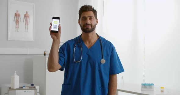 Male Doctor or Nurse Holding Smartphone with Virtual Immunity Passport in Clinic alt