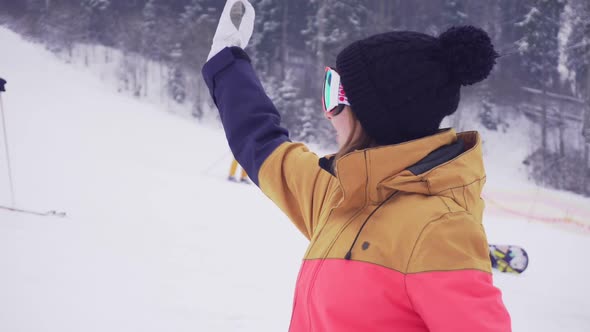 Young Sporty Woman in Ski Glasses Smiling and Waving with Her Hand Calling Someone alt