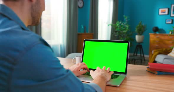 Over the Shoulder Shot of Mens Hands Typing on a Laptop with Green Mockup Screen alt