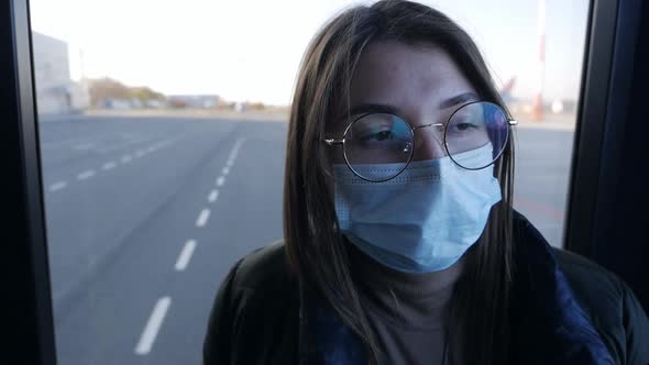 A Young Woman in a Protective Mask Rides an Airport Bus