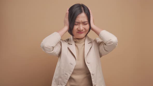 Asian business woman sad and annoyed covering her ears standing isolated over beige background.