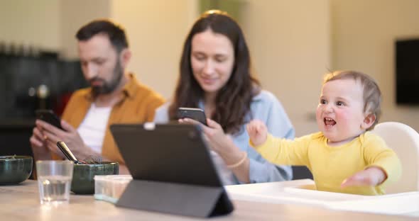 Baby and Parents Busy in a Digital Gadgets During a Lunch at Home alt