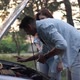 Side View Portrait of Focused Man Leaning at Open Car Hood Talking with Woman Standing at Background - VideoHive Item for Sale