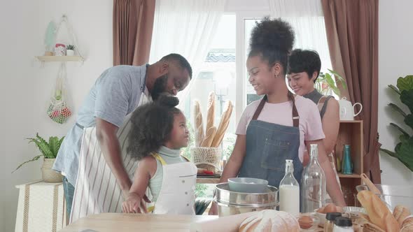 Happy moment. African American parents wearing aprons on little girls in kitchen at home.