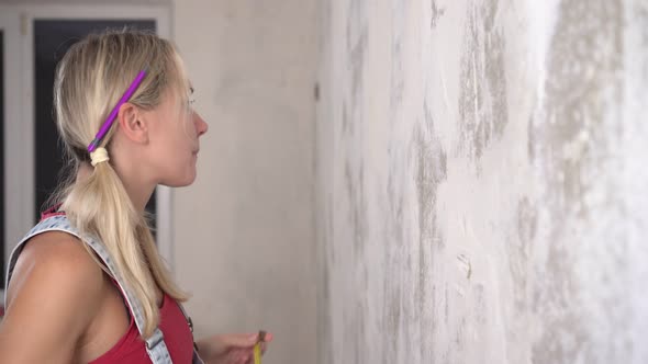 A Woman Makes Repairs and Measures the Wall with a Construction Tape alt